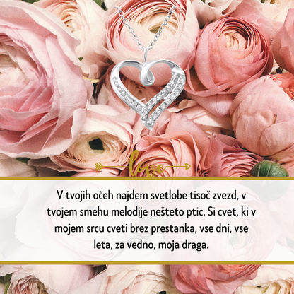 Personalizirana srebrna verižica z vgraviranim imenom in datumom, obdana z majhnimi kristali, kot idealno darilo za Dan žena. Elegantna darilna škatla na beli podlagi z rdečo vrtnico ob strani, simbolizira ljubezen in spoštovanje na poseben dan